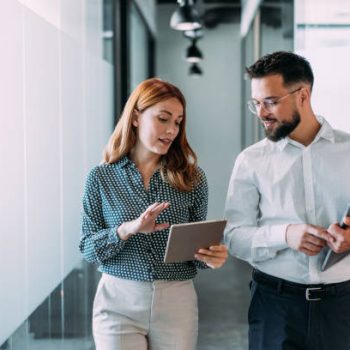 Shot of two coworkers having a discussion in modern office. Businessman and businesswoman in meeting using digital tablet and discussing business strategy. Confident business people working together in the office. Creative business persons discussing new project and sharing ideas in the workplace.